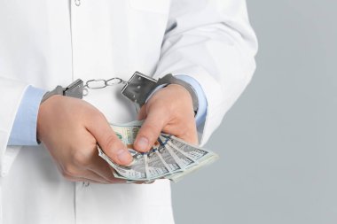 Gri arka planda rüşvetle kelepçelenmiş bir doktor, yakın plan. Corr