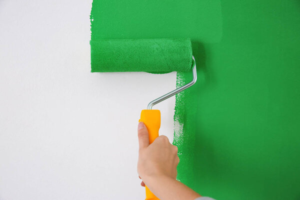 Woman painting white wall with green dye, closeup. Interior renovation