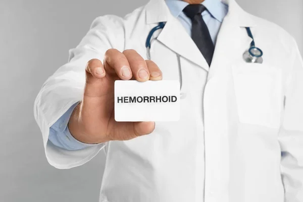 医者の名刺を持っている単語Hemorroidライトグレーの背景に クローズアップ — ストック写真