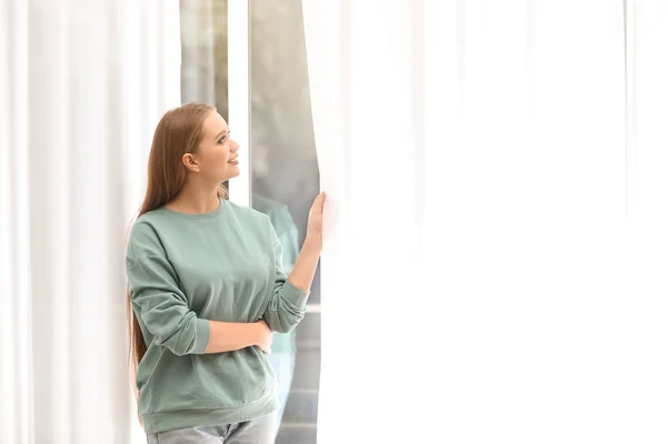 Güzel genç kadın evde pencereden dışarı bakıyor — Stok fotoğraf