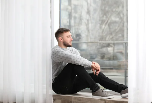 Handsome young man near window at home — Stock Photo, Image