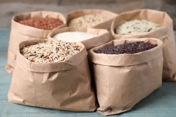 Brown and polished rice in paper bags on blue wooden table