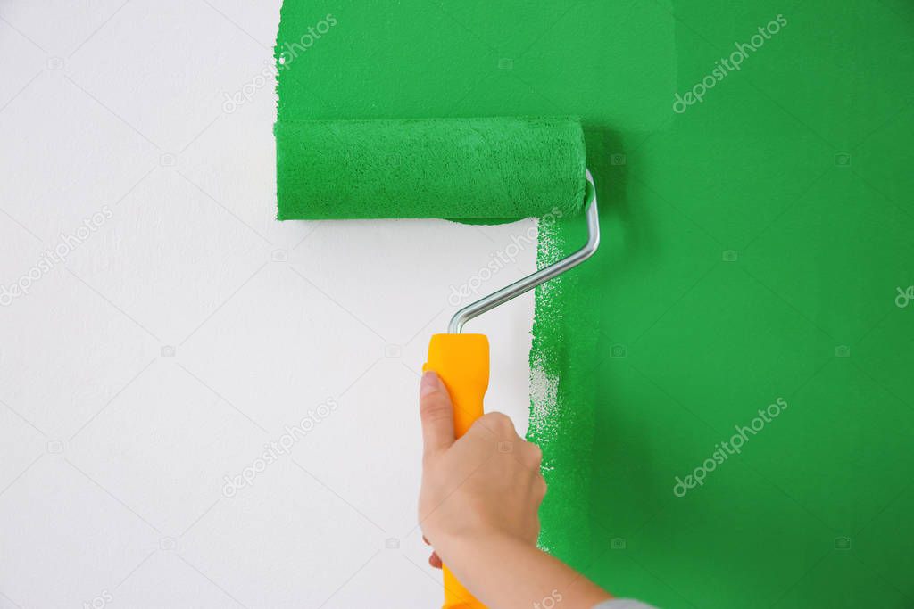 Woman painting white wall with green dye, closeup. Interior renovation