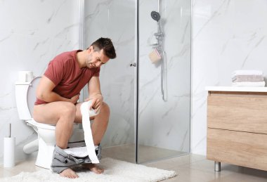 Tuvaletteki klozette mide ağrısı çeken kağıt rulolu bir adam.