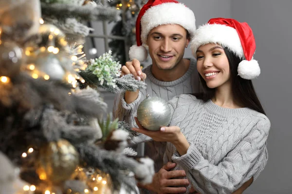 Šťastný Mladý Pár Santa Klobouky Zdobení Vánoční Stromeček Společně Doma — Stock fotografie