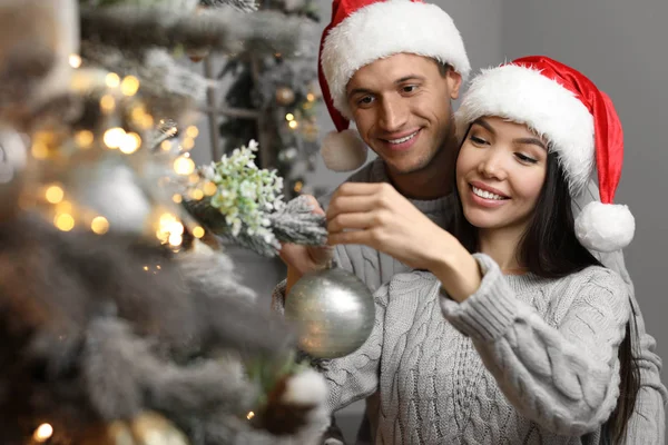 幸せな若いですカップルでサンタ帽子装飾クリスマスツリー一緒に家で — ストック写真