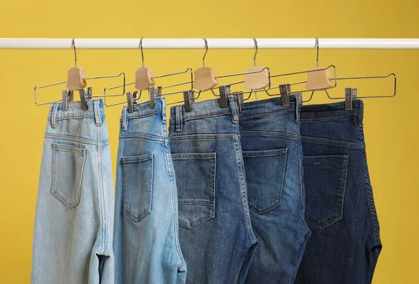Stojak z różnymi dżinsami na żółtym tle — Zdjęcie stockowe
