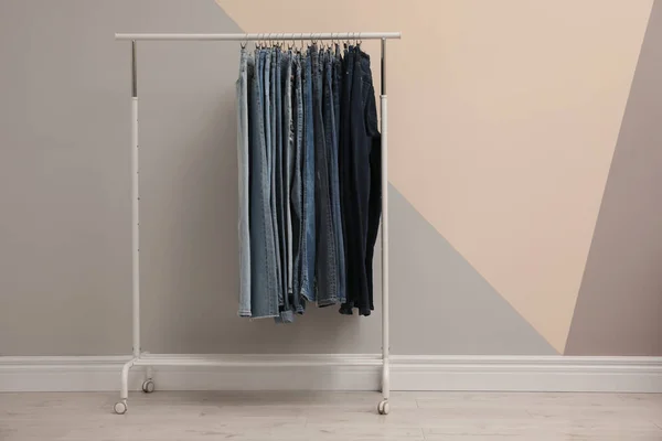 Rack met stijlvolle jeans in de buurt van kleur muur. Ruimte voor tekst — Stockfoto