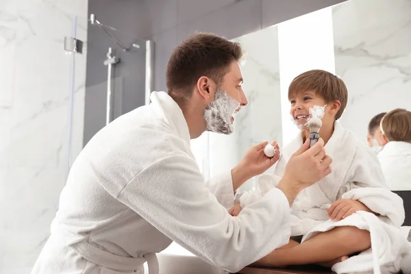 Papá aplicando espuma de afeitar en la cara del hijo en el baño — Foto de Stock