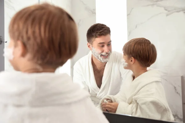 Vader en zoon met scheerschuim op gezichten in de badkamer — Stockfoto