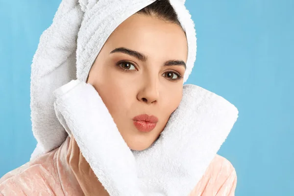 Young woman wiping face with towel on light blue background