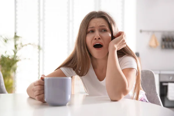 Sleepy young woman with cup of drink at home in morning — ストック写真