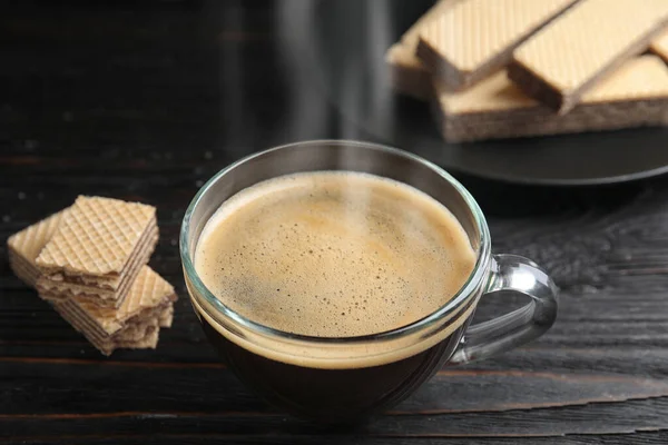 Delicious coffee and wafers on black wooden table