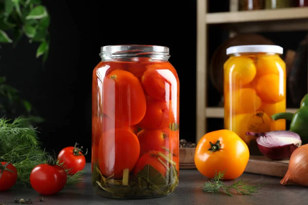 Glass jars of pickled tomatoes on grey table — 스톡 사진