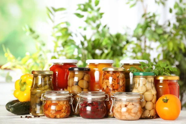 Pots en verre de différents légumes marinés sur table en bois blanc — Photo