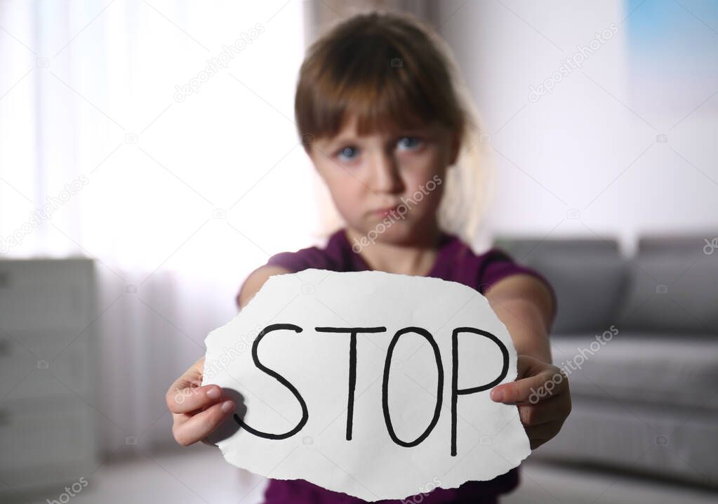 Abused little girl with sign STOP indoors, focus on hands. Domes