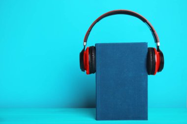Book and modern headphones on light blue wooden table. Space for clipart