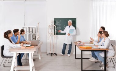 Tıp öğrencileri ve profesör sınıfta insan iskeleti anatomisi okuyor.