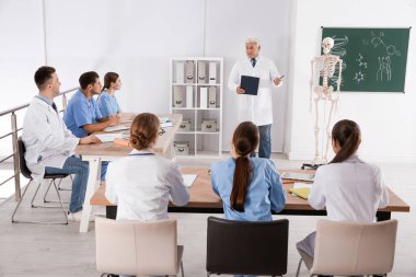 Tıp öğrencileri ve profesör sınıfta insan iskeleti anatomisi okuyor.