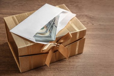 Tahta masanın üzerinde dolar banknotları olan bir hediye kutusu.