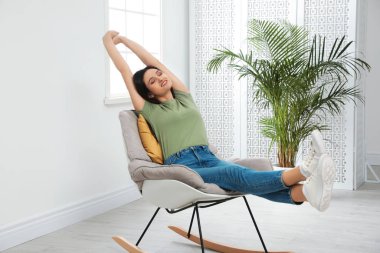 Evde sallanan sandalyede dinlenen genç bir kadın.