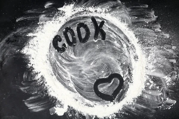 Heart and word COOK written on flour scattered over black table, top view