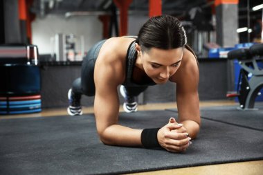 Modern spor salonunda tahta egzersizi yapan genç bir kadın.