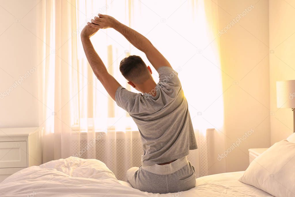 Young man stretching on bed at home, view from back. Lazy morning