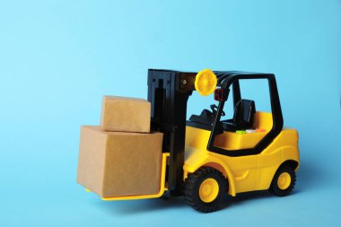Mavi arka planda kutuları olan oyuncak forklift. Lojistik ve toptan satış kavramı