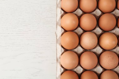 Beyaz ahşap masada çiğ tavuk yumurtası, üst manzara.