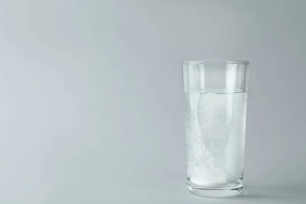 Glass of water with effervescent tablet on light grey background, space for text