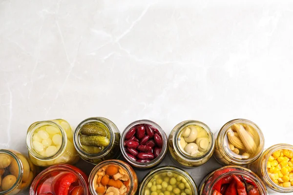 Скляні банки з різними маринованими овочами на світло-сірому мармурі — стокове фото