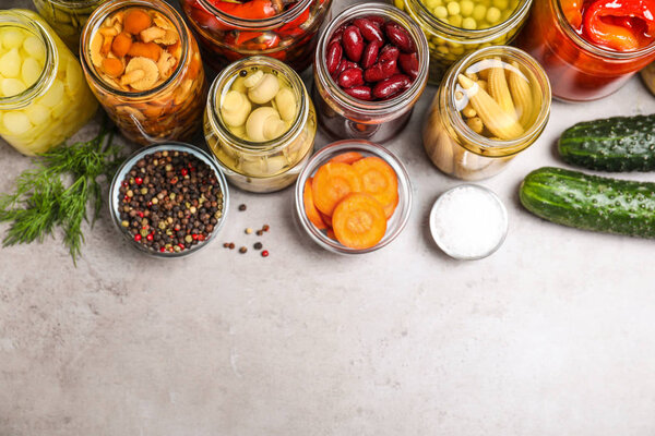 Glass jars with different pickled vegetables on grey table, flat