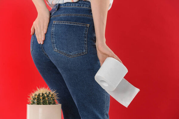 Woman with toilet paper sitting down on cactus against red background, closeup. Hemorrhoid concept