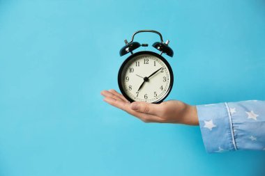 Açık mavi arka planda alarmlı saat tutan kadın, yakın plan. Sabah oldu.