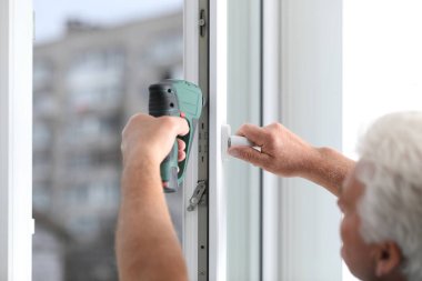 İnşaat işçisi plastik pencereyi elektrikli tornavidayla tamir ediyor.