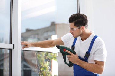 İnşaat işçisi plastik pencereyi elektrikli tornavidayla tamir ediyor.