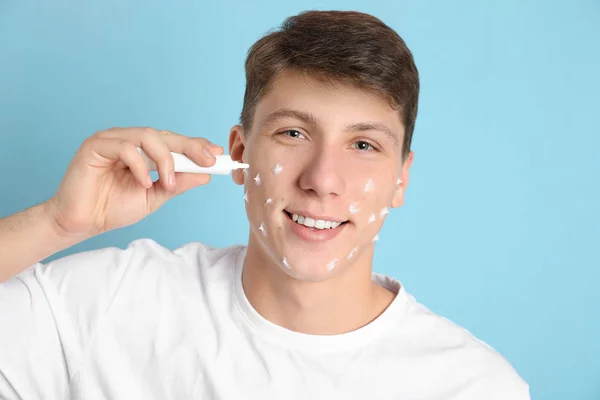 Adolescent guy avec acné problème application crème sur lumière bleu backgrou — Photo