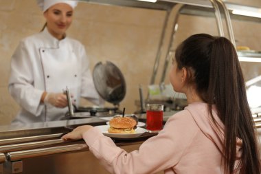 Mataranın yanında plastik tepsiyle servis yapan küçük bir kız. Okul yemeği.
