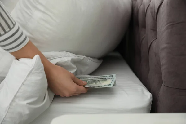 Woman hiding dollar banknotes under pillow in bedroom, closeup. Money savings