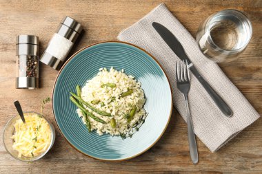 Delicious risotto with asparagus served on wooden table, flat lay