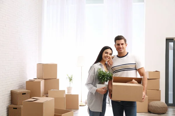 Pareja feliz en la habitación con cajas de cartón en el día en movimiento —  Fotos de Stock