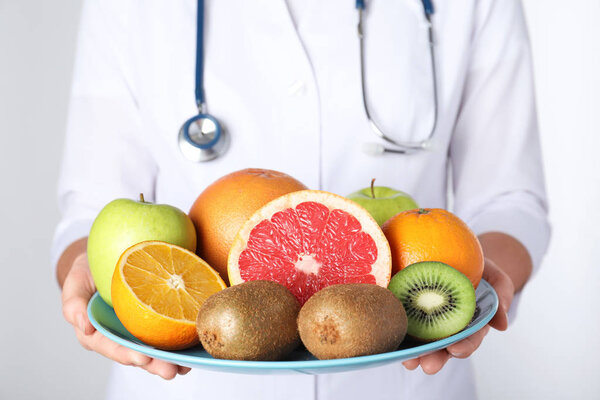 Female nutritionist with fruits on light background, closeup