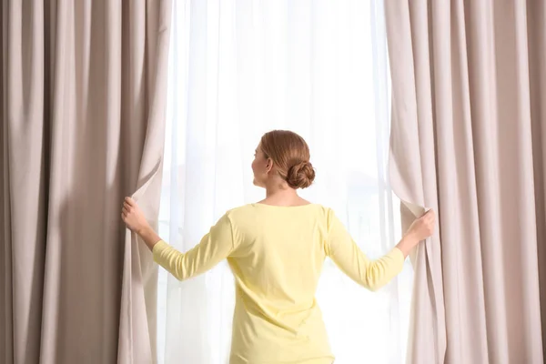 朝家で窓のカーテンを開ける女 — ストック写真