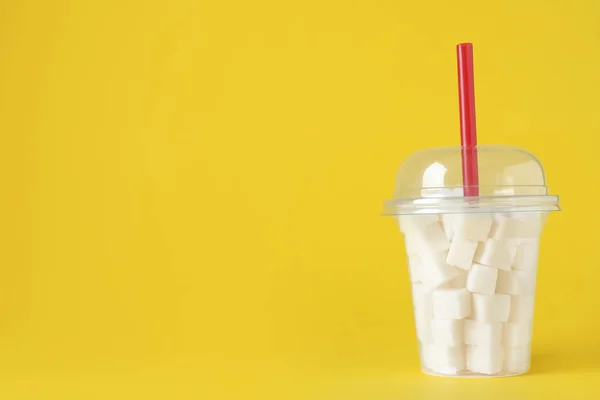 Refined sugar cubes in plastic cup with straw on yellow backgrou — Stock Photo, Image
