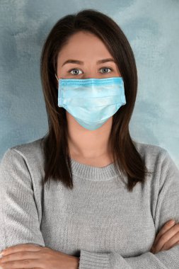 Yüzü açık mavi arka planda tek kullanımlık maskeli kadın