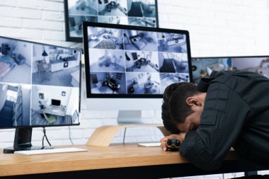 İş yerindeki monitörlerin yanında uyuyan erkek güvenlik görevlisi