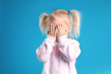 Açık mavi arka planda poz veren şirin küçük kız.