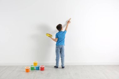 Beyaz duvarlara resim yapan küçük bir çocuk.