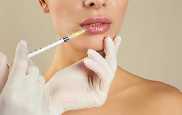 Woman getting lip injection on beige background, closeup